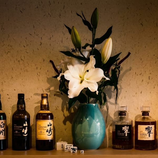 A collection of Japanese whisky bottles, including Yamazaki and Hibiki, displayed with a white lily arrangement.