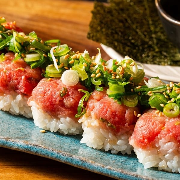Five pieces of nigiri sushi with minced red tuna, green onions, and sesame seeds on a blue plate.