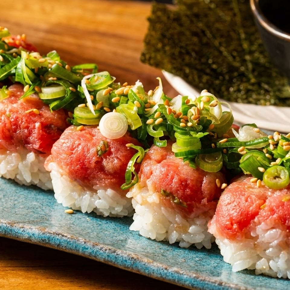 Five pieces of nigiri sushi with minced red tuna, green onions, and sesame seeds on a blue plate.