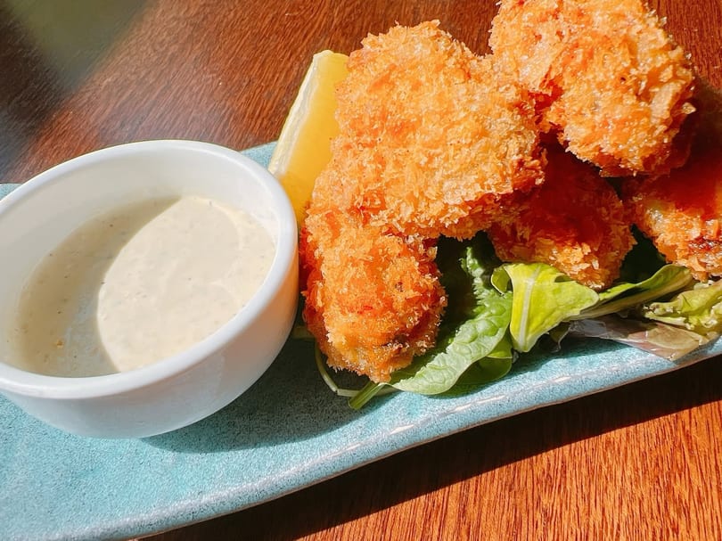 Crispy fried oysters with a lemon wedge, lettuce, and a side of creamy dipping sauce.