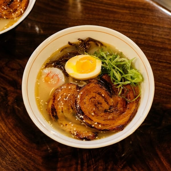 Two bowls of ramen with pork, egg, and green onions on a dark wooden table.