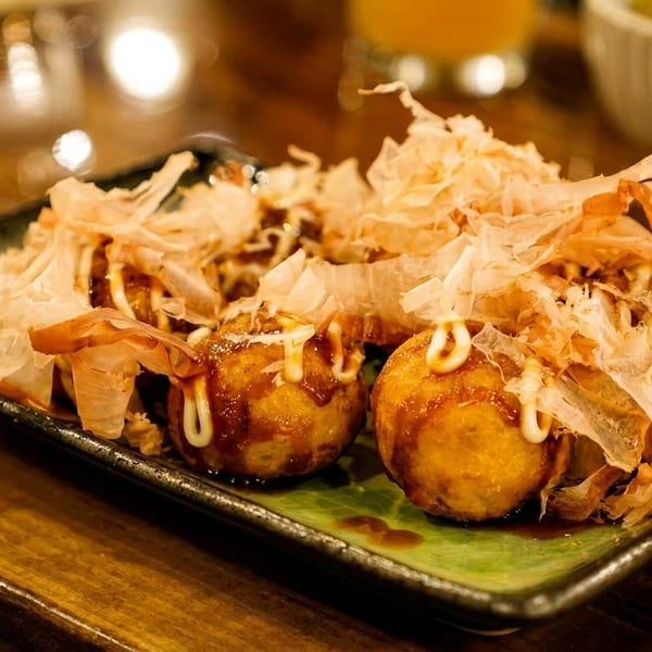 Close-up of takoyaki topped with bonito flakes and mayonnaise on a green and black plate.