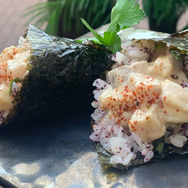Two temaki hand rolls with creamy filling, rice, and red spice on a dark plate.
