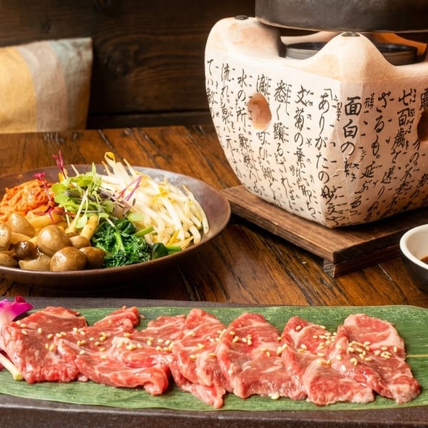 Raw beef slices, a side dish of vegetables and mushrooms, and a decorative pot on a wooden table.