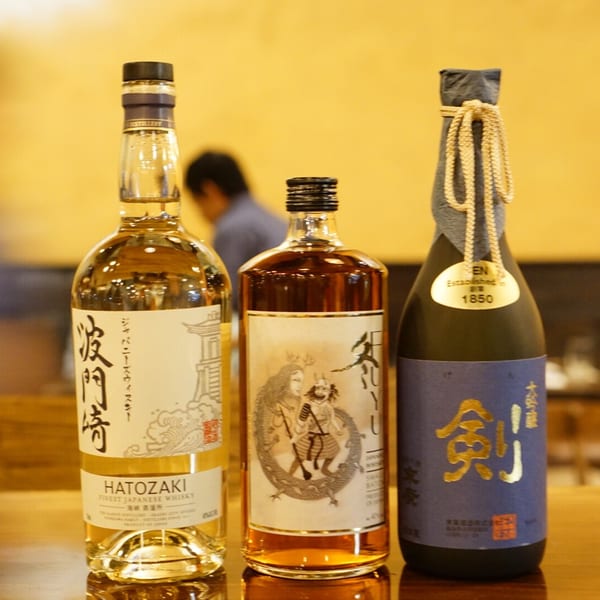 Three bottles of Japanese spirits, including Hatozaki whisky and sake, on a wooden surface.