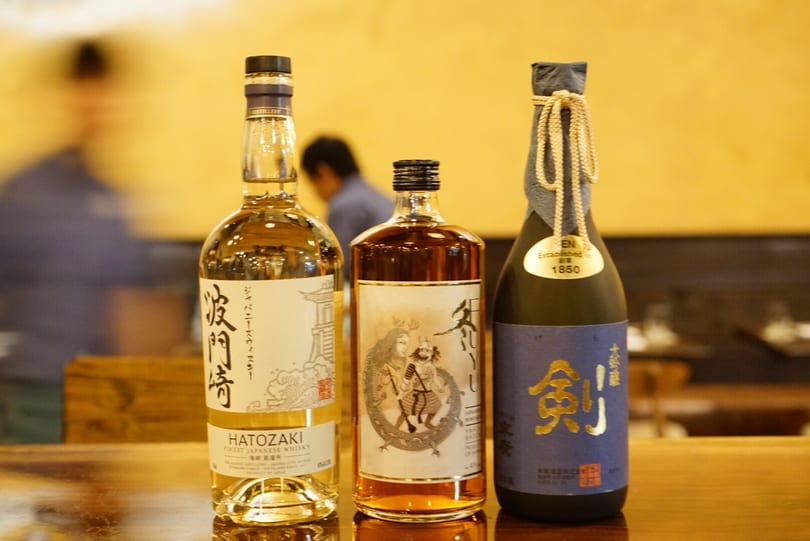 Three bottles of Japanese spirits, including Hatozaki whisky and sake, on a wooden surface.