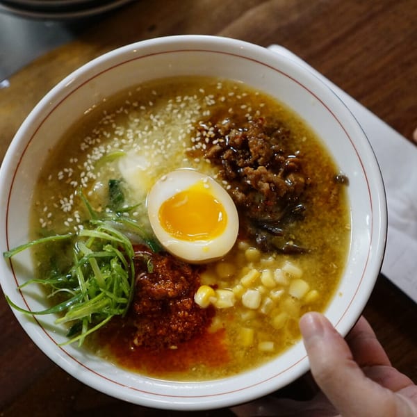 Overhead view of a ramen bowl with a soft-boiled egg, corn, scallions, and ground meat.