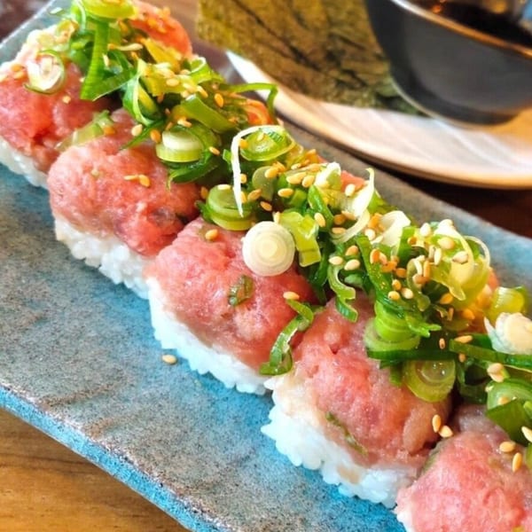 Close-up of sushi rolls with tuna, green onions, and sesame seeds on a blue plate.