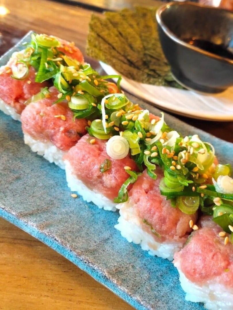 Close-up of sushi rolls with tuna, green onions, and sesame seeds on a blue plate.