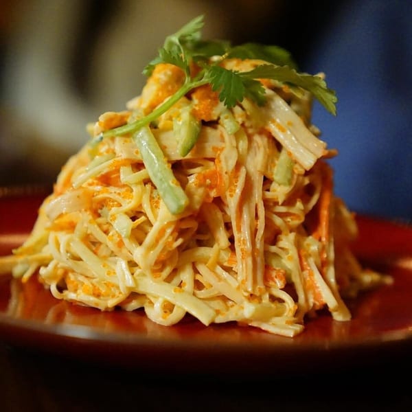 A vibrant crab salad with tobiko, avocado, and cilantro, served on a red plate.