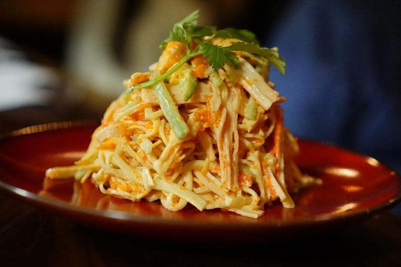 A vibrant crab salad with tobiko, avocado, and cilantro, served on a red plate.